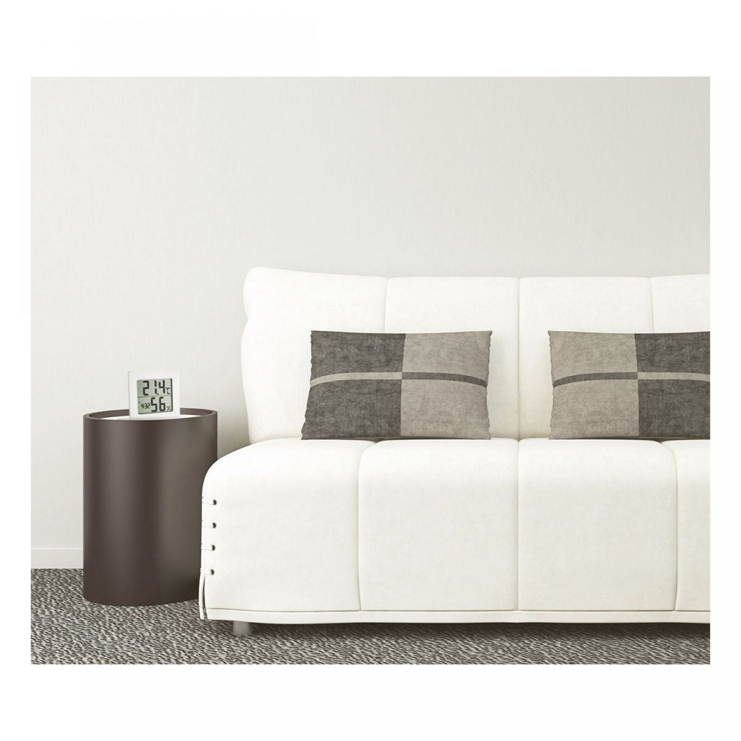 Eine weiße Couch mit karierten Kissen und ein brauner Beistelltisch mit Uhr darauf.