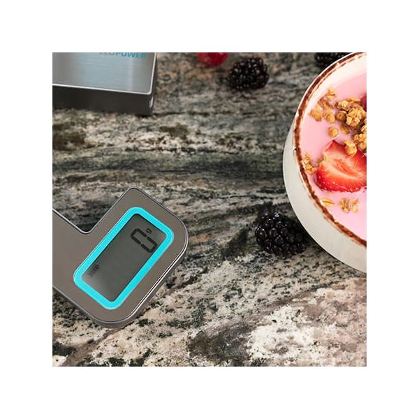 Cyfrowa waga kuchenna z jogurtem i jagodami na marmurowej powierzchni.