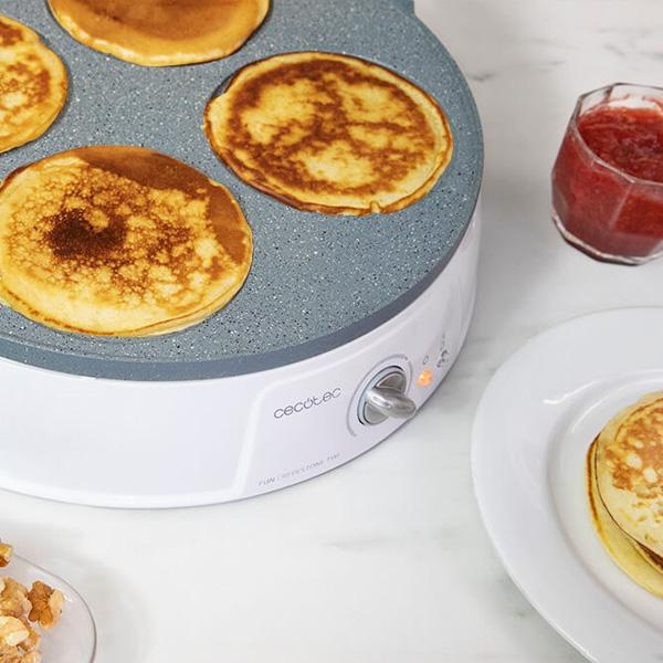 Pannenkoeken op een bakplaat. Wit bord met siroop. Pot jam. Marmeren aanrecht.