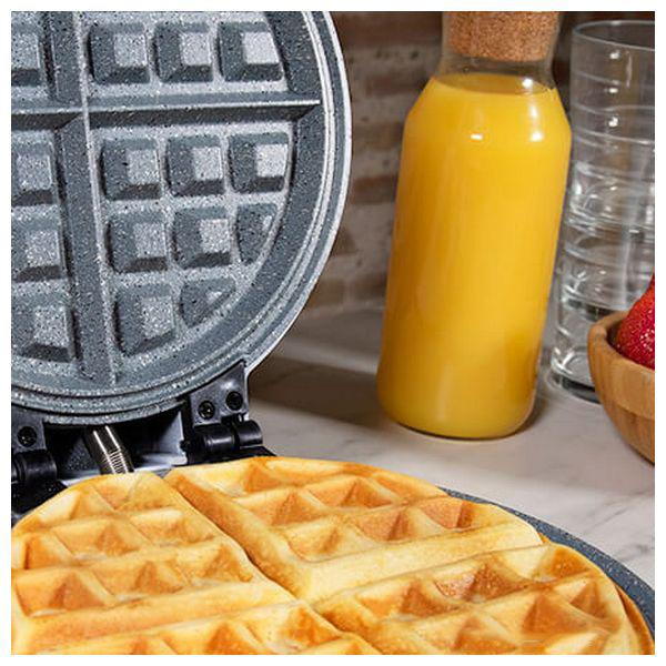 Waffeln auf einem Waffeleisen, mit einer Flasche Orangensaft und einer Schüssel Erdbeeren.
