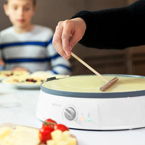 Een persoon gebruikt een houten tool om beslag op een crêpe maker te smeren. Een jongen op de achtergrond.