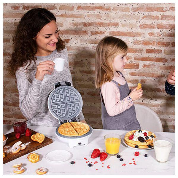 Eine Frau und ein Kind machen Waffeln. Auf einem Tisch liegen Waffeln, Obst und Saft.