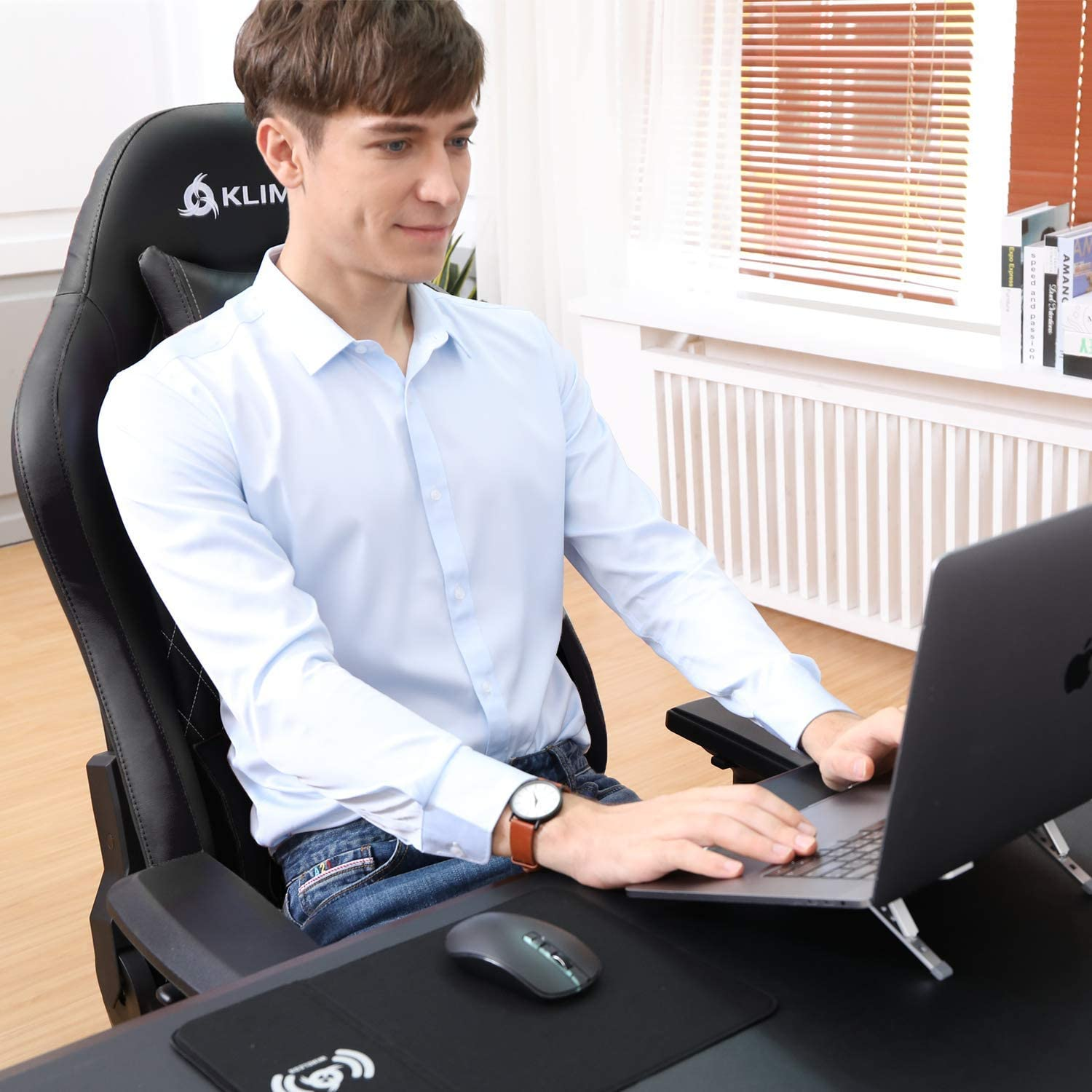 Ein Mann in blauem Hemd sitzt in einem schwarzen Gaming-Stuhl und benutzt einen Laptop.