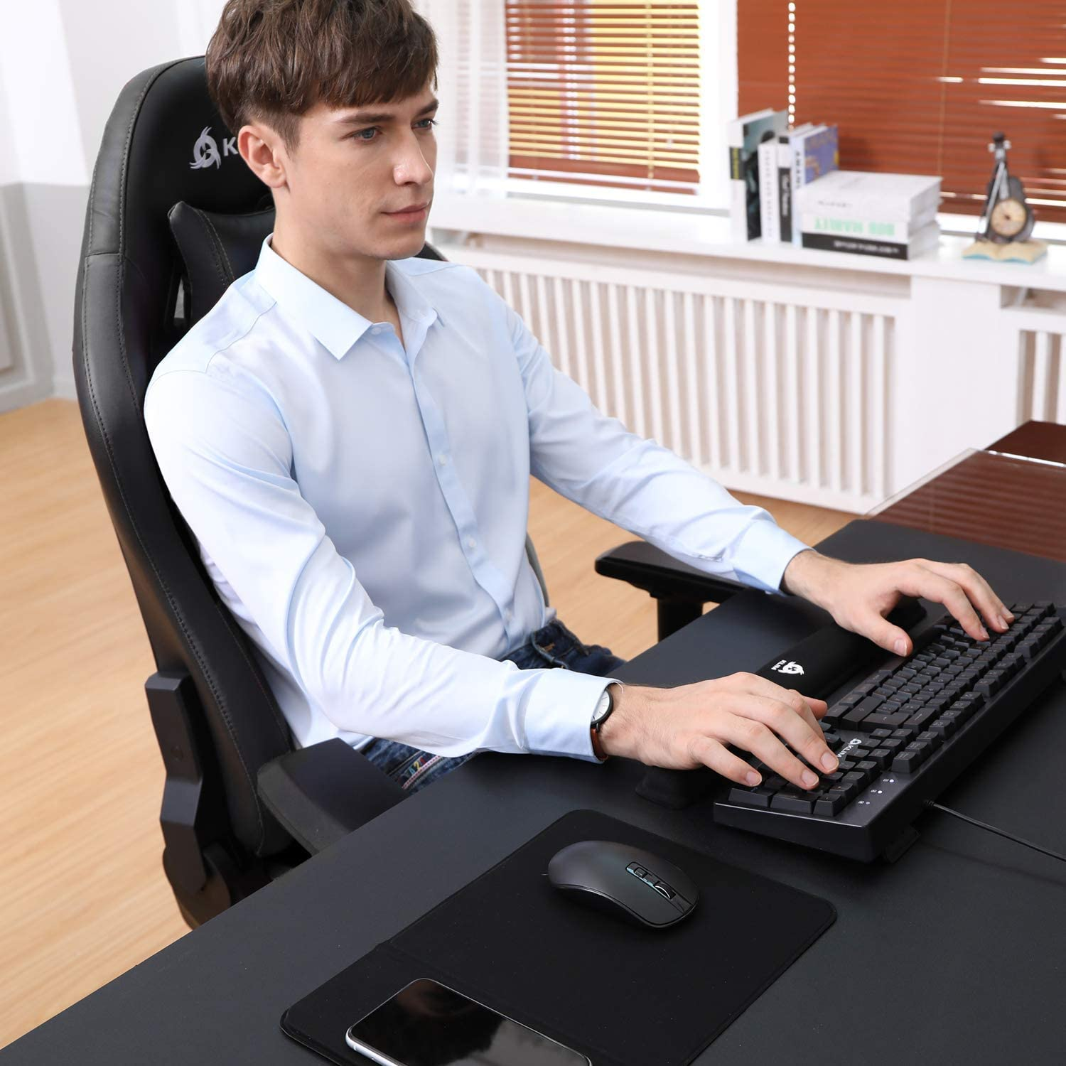 Mann benutzt Computer. Er trägt hellblaues Hemd, sitzt in Gaming-Stuhl.