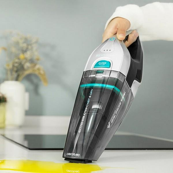 Eine Hand hält einen grau-schwarzen Staubsauger. Auf der Theke befindet sich eine gelbe Flüssigkeit.