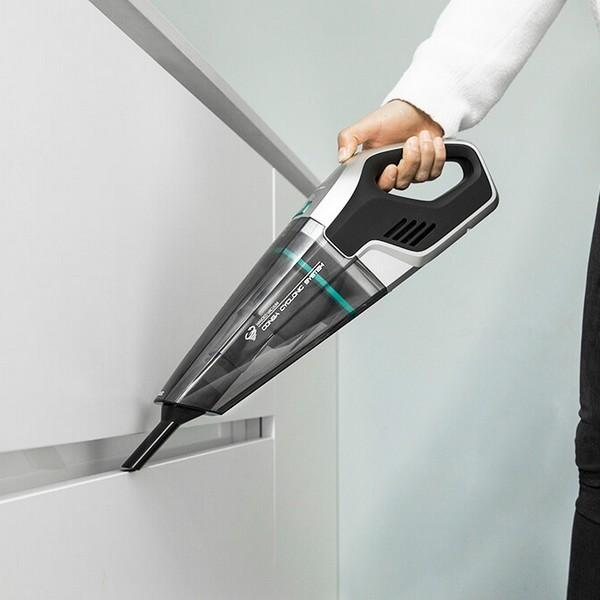 Eine Person verwendet einen schwarz-silbernen Handstaubsauger, um einen weißen Schrank zu reinigen.