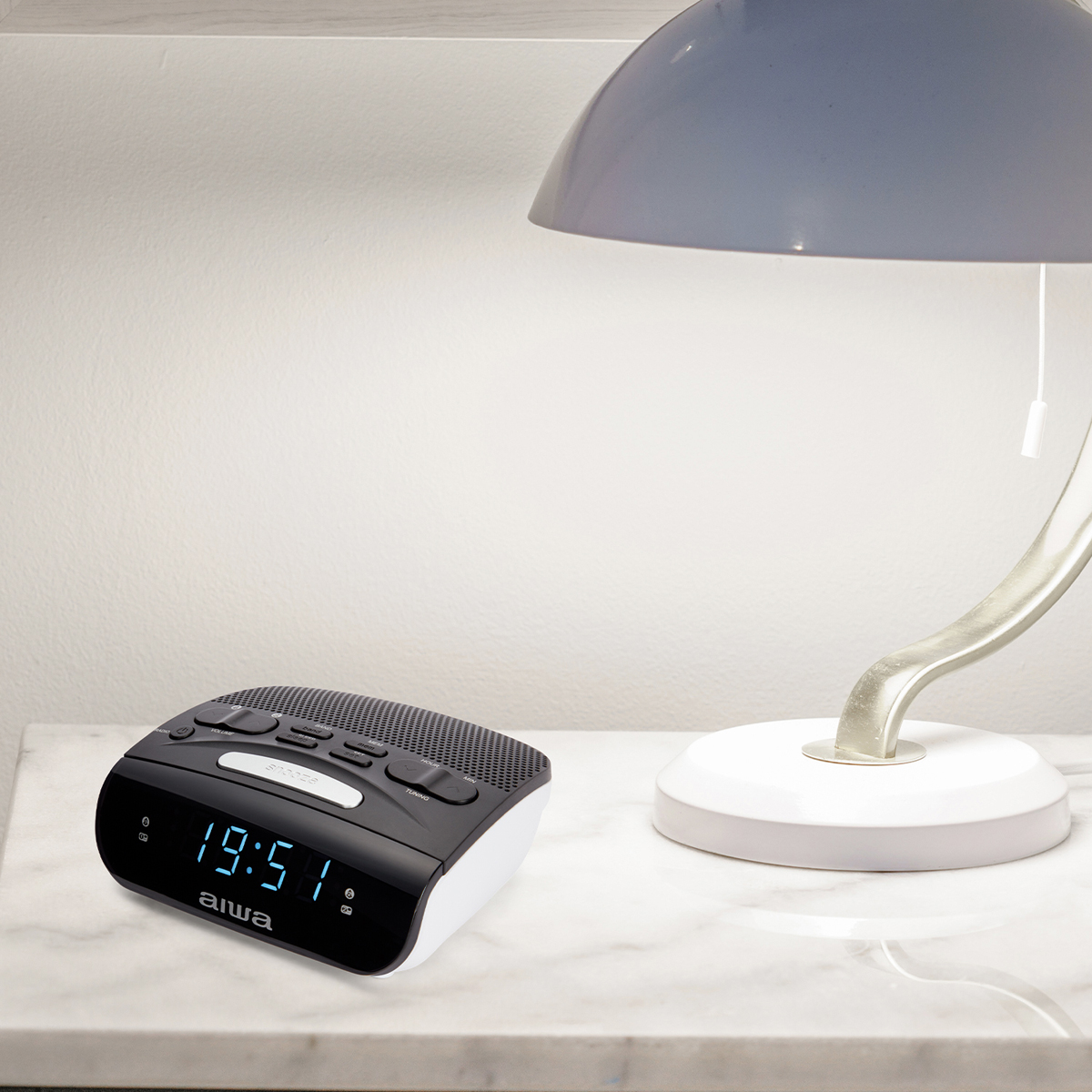 Czarno-białe radiobudzik Aiwa na marmurowej powierzchni, z niebieską lampą w tle.