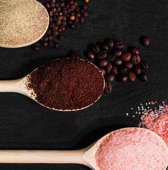 Drewniane łyżki z mieloną kawą, ziarnami pieprzu, ziarnami kawy i różową solą.