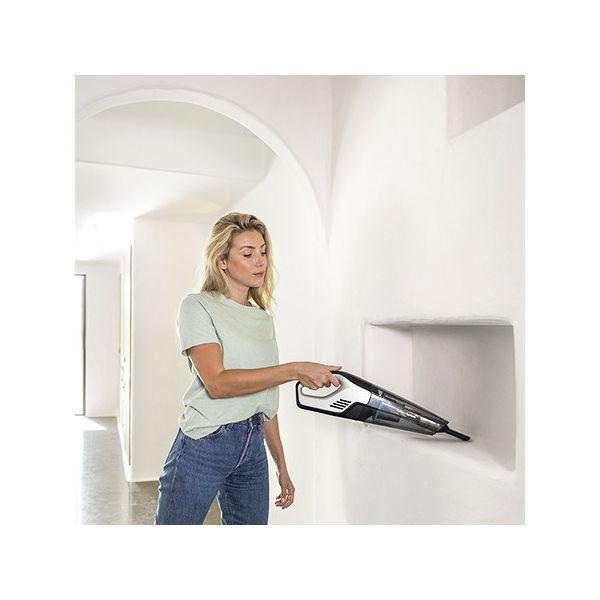Donna che aspira un muro bianco con un aspirapolvere portatile.