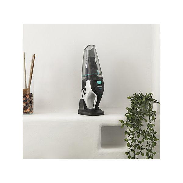 Piccolo aspirapolvere su uno scaffale. Aspirapolvere bianco e nero su uno scaffale bianco con piante e decorazioni.