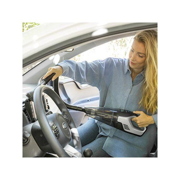 Eine Frau saugt mit einem Handstaubsauger den Innenraum eines Autos. Sie sitzt im Auto.