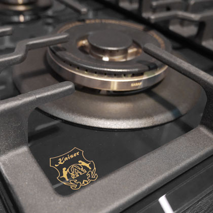 Nahaufnahme eines Gasherd-Brenners mit schwarzer Oberfläche. Ein goldenes 'Kaiser'-Logo ist sichtbar.