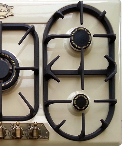 Primer plano de una encimera de gas color crema con rejillas negras y perillas color latón.