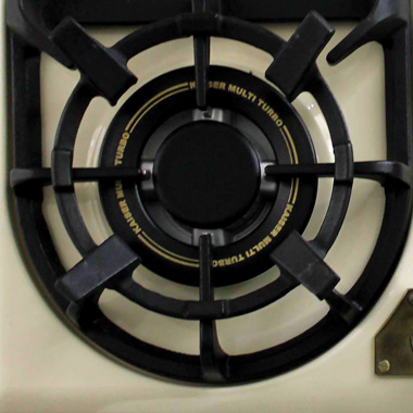 Primer plano de un quemador de cocina a gas. Rejilla y quemador de metal negro con detalles dorados.