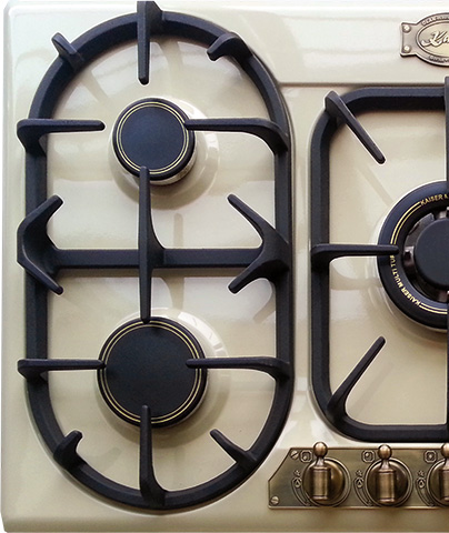 Primer plano de una cocina de gas con parrillas negras y mandos de latón. Marca Kaiser & Kaiser Built visible.