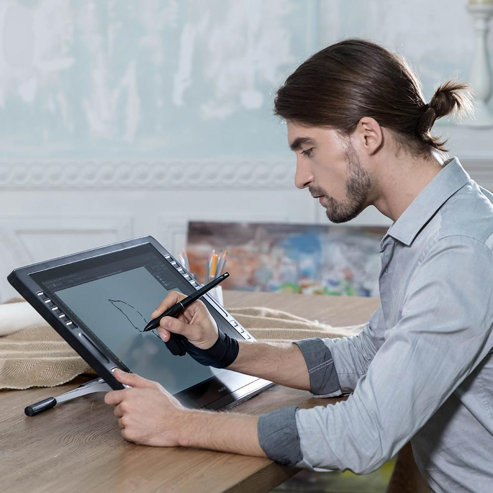 Ein Mann, der ein digitales Zeichentablett benutzt, mit einem Stift zeichnet, mit Staffelei und Gemälden im Hintergrund.
