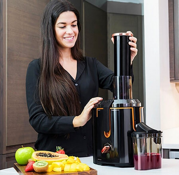 Donna che usa un estrattore di succo, con frutta su un tagliere e succo in un contenitore.