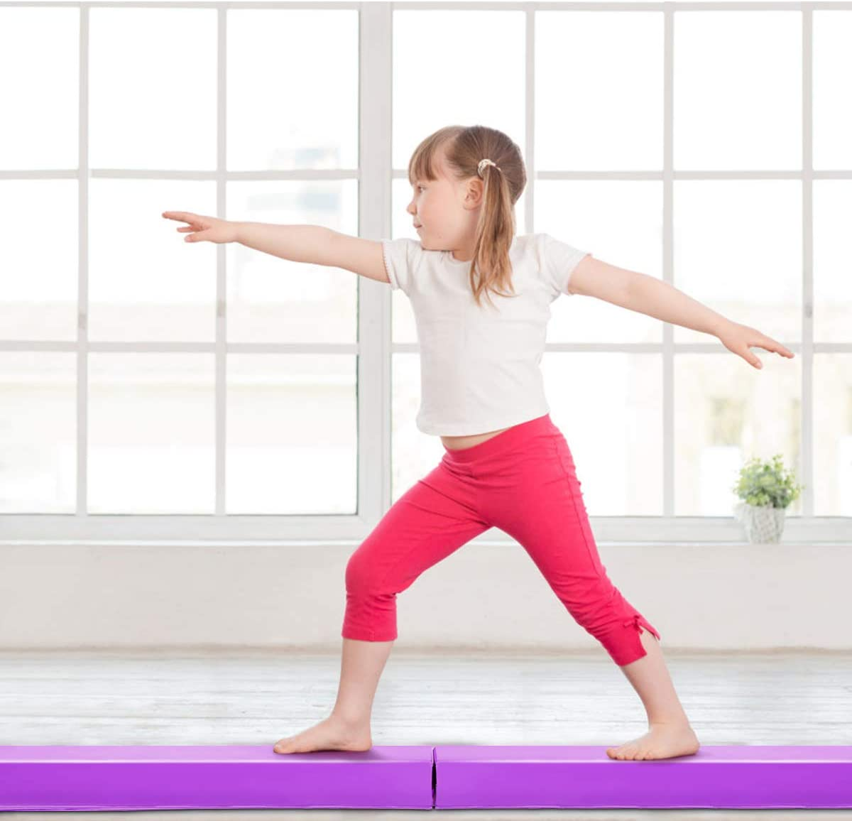Junges Mädchen macht Yoga auf einer lila Matte mit Fenster im Hintergrund.