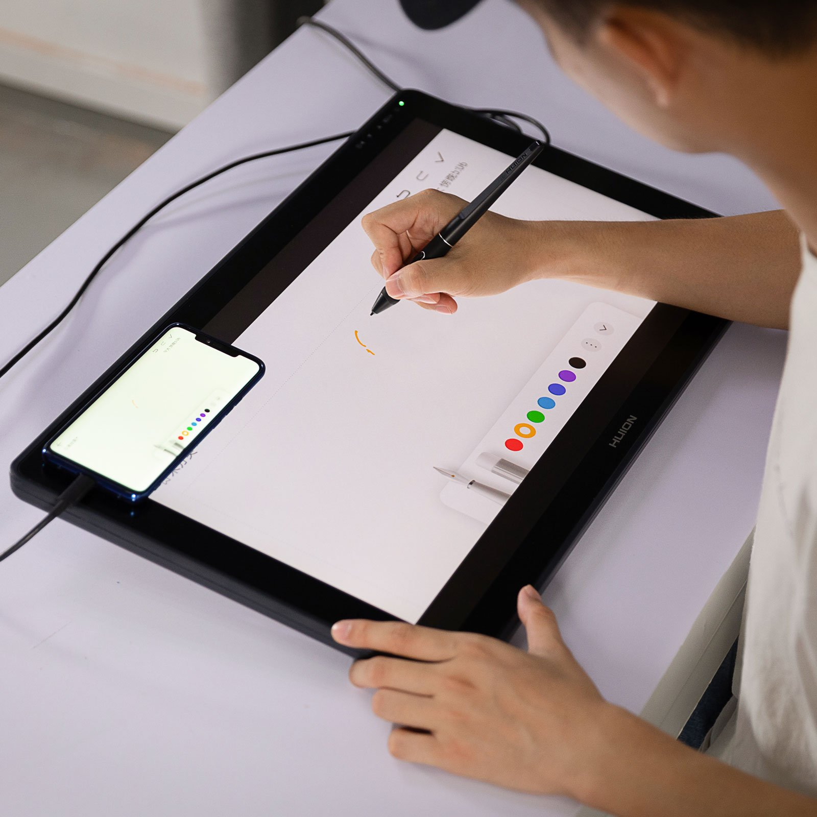 Eine Person benutzt ein Tablet-Gerät und zeichnet mit einem Stift. Ein Telefon befindet sich neben dem Tablet. Farbpalette.
