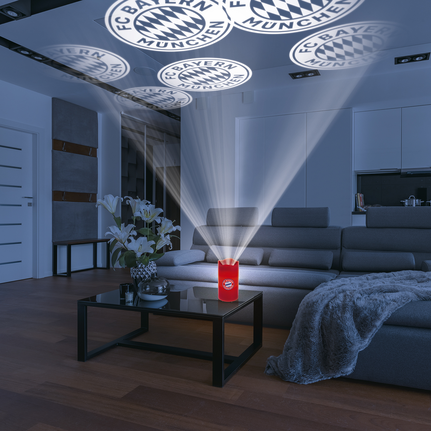Ein Raum mit einem Projektor, der das Bayern München-Logo an die Decke projiziert. Ein rotes Licht scheint auf einen Tisch.