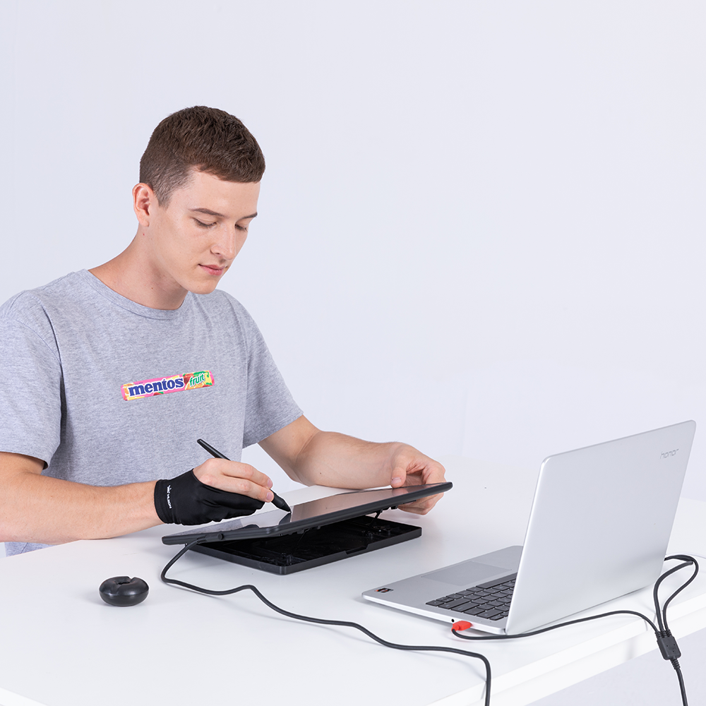 Mężczyzna używający pióra na tablecie do rysowania, laptopie i myszy na białym stole.