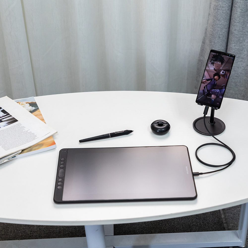 Tablet, telefon na stojaku i długopis na białym stole. Scena jest jasno oświetlona.