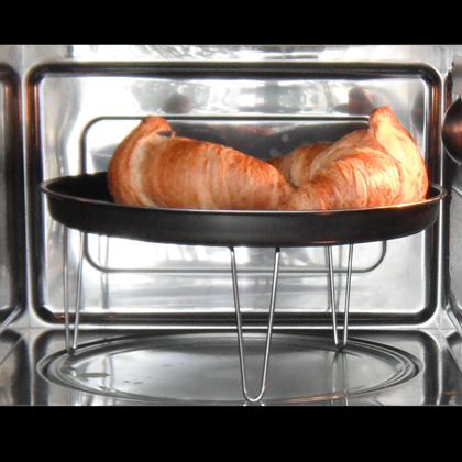 Zwei Croissants auf einem schwarzen Metallgestell in einem Mikrowellenofen. Der Ofen ist aus Edelstahl.
