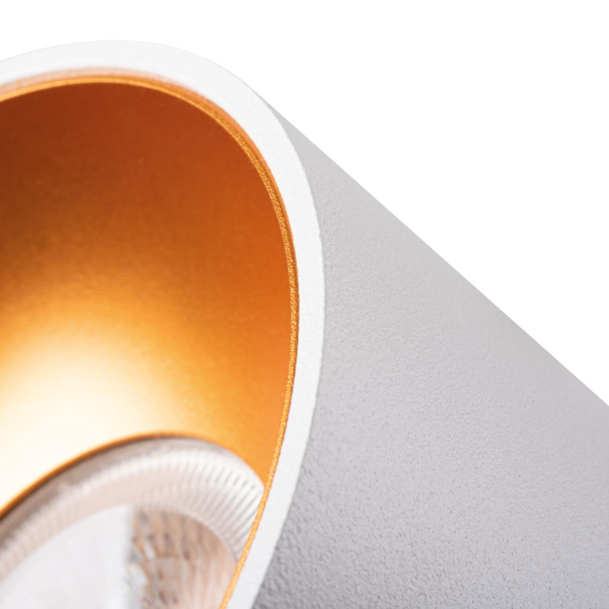 Un primo piano di un apparecchio di illuminazione bianco e oro. L'interno della luce è dorato.