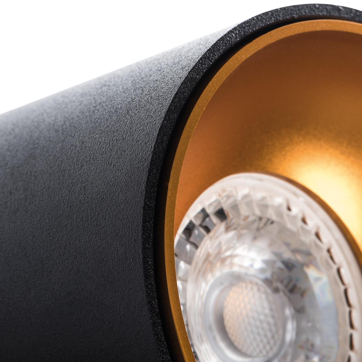 Primo piano di una luce nera e oro. La luce è incassata, con una lampadina brillante all'interno.
