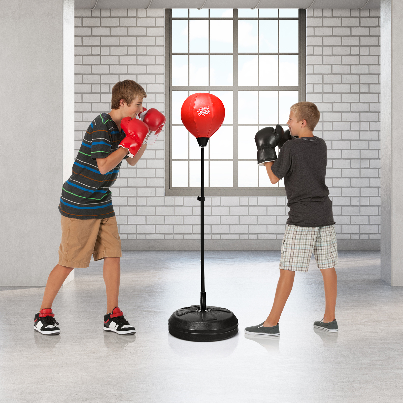 Zwei Jungen boxen mit Handschuhen in einem Raum. Zwischen ihnen steht ein roter Boxsack.