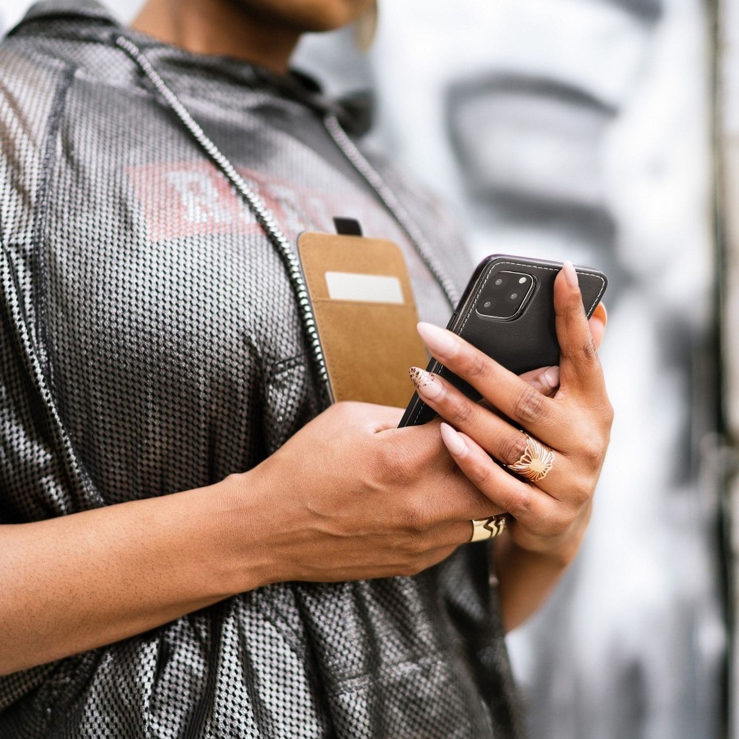 Eine Person hält ein schwarzes Telefon mit einer braunen Brieftaschen-Handyhülle, die einen goldenen Ring und lange Nägel zeigt.