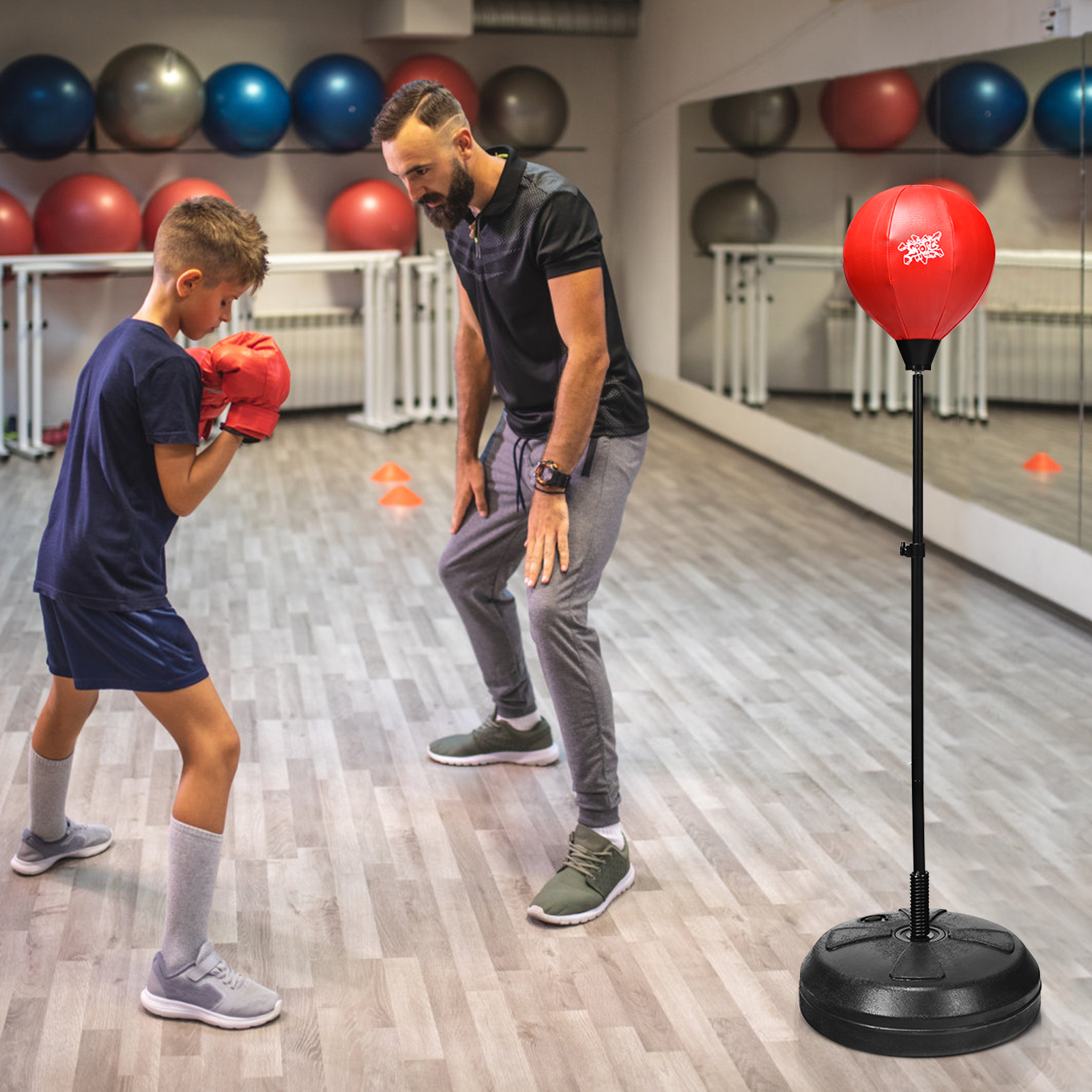 Junge boxt. Mann beobachtet, roter Boxsack im Hintergrund. Fitnessstudio.
