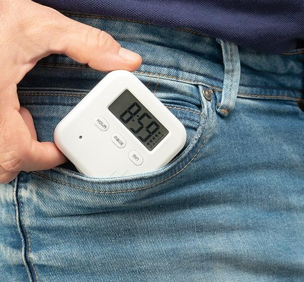 Ein weißer quadratischer digitaler Timer in einer Jeanstasche. Auf dem Bildschirm steht 8:59.