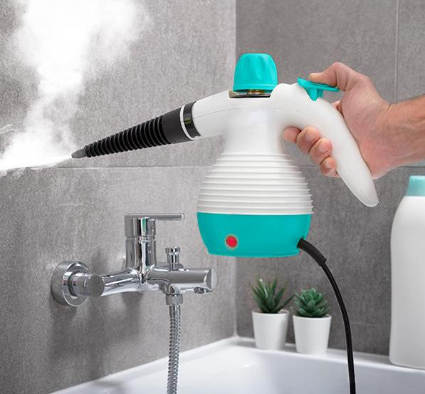 Handdampfreiniger auf einem Waschbecken mit Wasserhahn und kleinen Pflanzen.