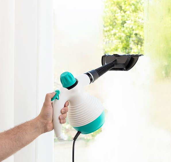 Hand hält einen Dampfreiniger und reinigt ein Fenster.