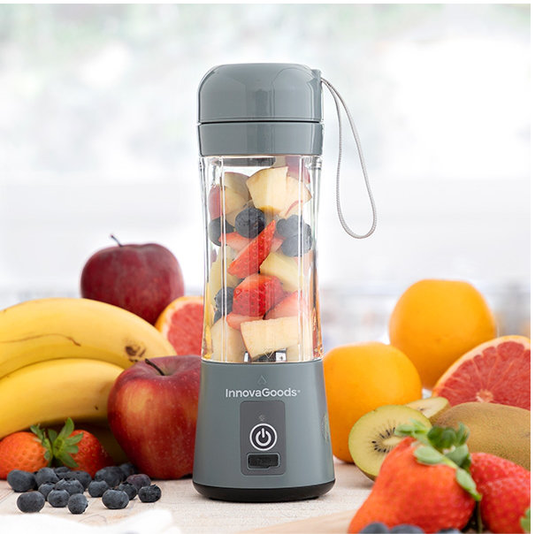 Szary przenośny blender wypełniony posiekanymi owocami. Ma białe tło.