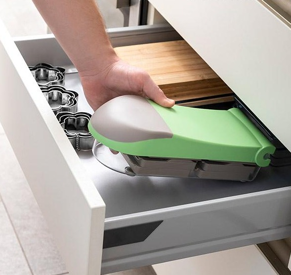 Una persona che mette un utensile da cucina in un cassetto. L'utensile è verde e grigio.