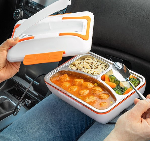 Lunchbox mit Fächern, gefüllt mit Essen und einem Löffel, in einem Auto.
