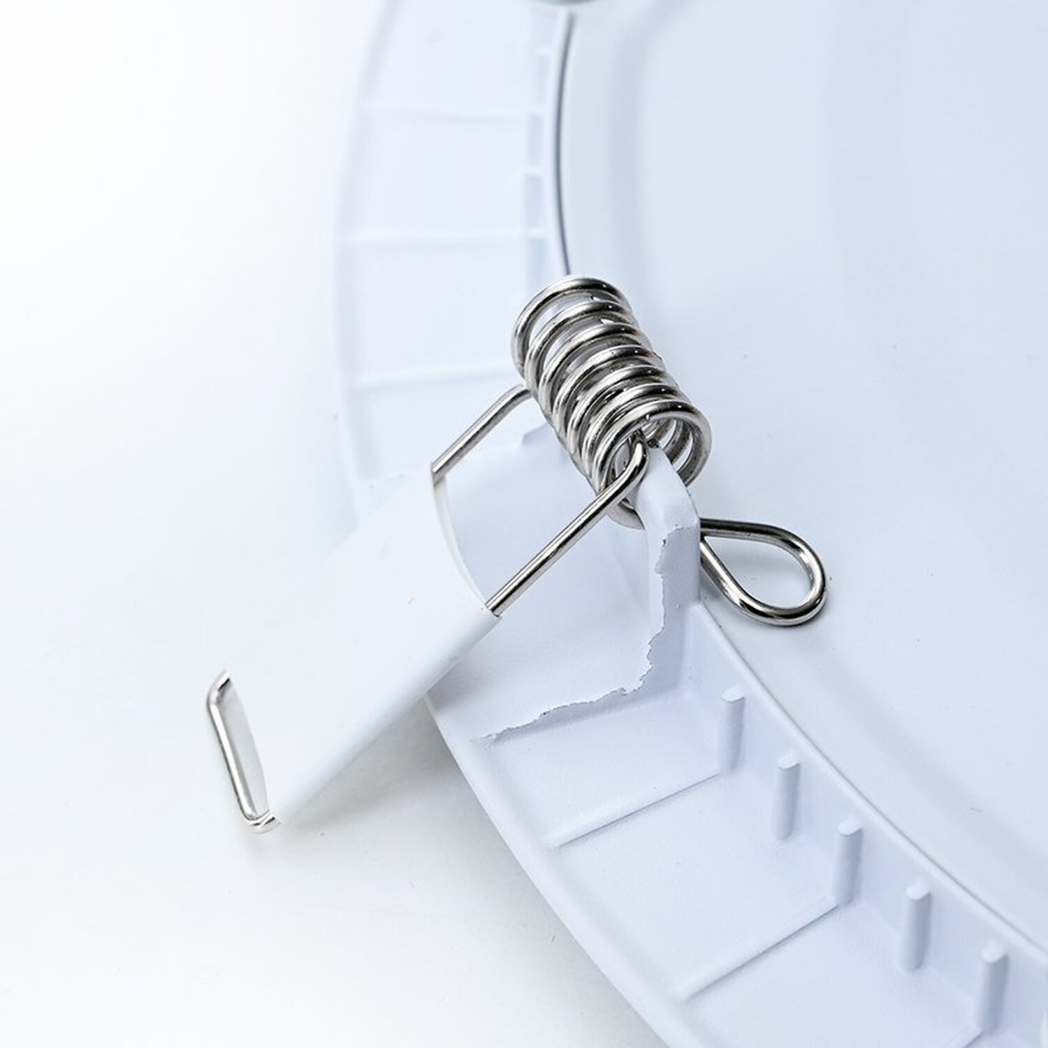 Weiße Deckenleuchtenkomponente mit Metallfederclip, der ein Kunststoffteil hält.