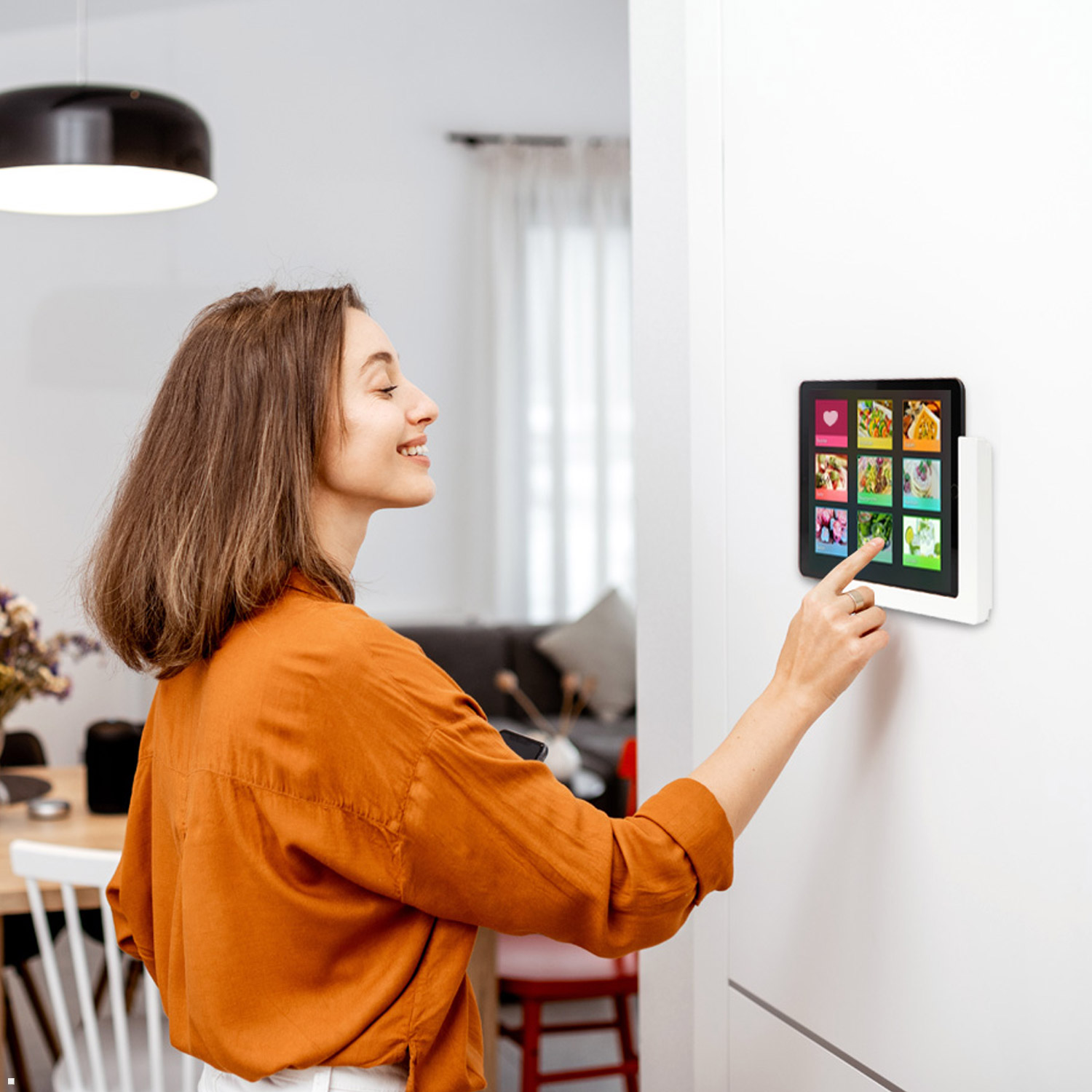 Frau interagiert mit einem wandmontierten Tablet, das Bilder zeigt.