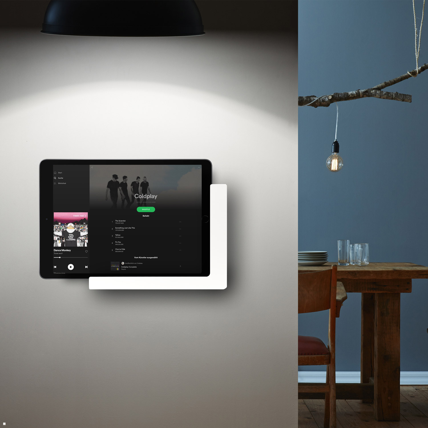 Tablet an einer Wandhalterung, Spotify-Playlist. Dunkle Lampe und Holztisch in der Nähe.