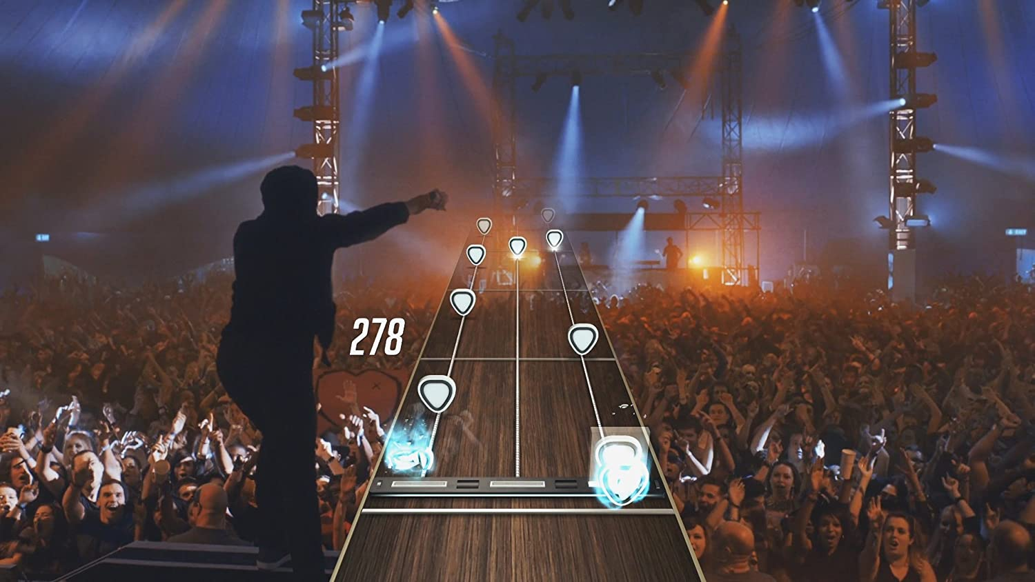 Eine Konzertbühne mit einer Silhouette einer Person, die ein Musikspiel spielt. Publikum im Hintergrund.