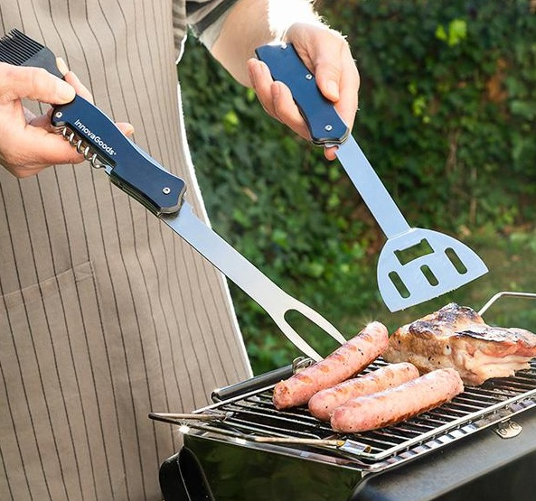 Person grillt Würstchen und Fleisch auf einem Grill. Zwei Grillwerkzeuge im Einsatz.