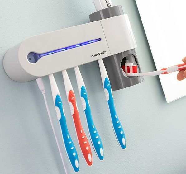 Un porta cepillos de dientes montado en la pared con cepillos de dientes y un dispensador de pasta dental. Un espejo está en el fondo.