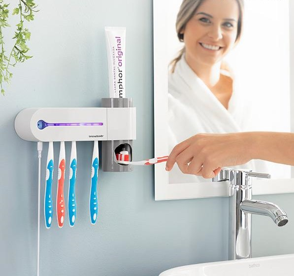 Una mujer usando un cepillo de dientes. Un dentífrico y un soporte para cepillos de dientes están en la pared.