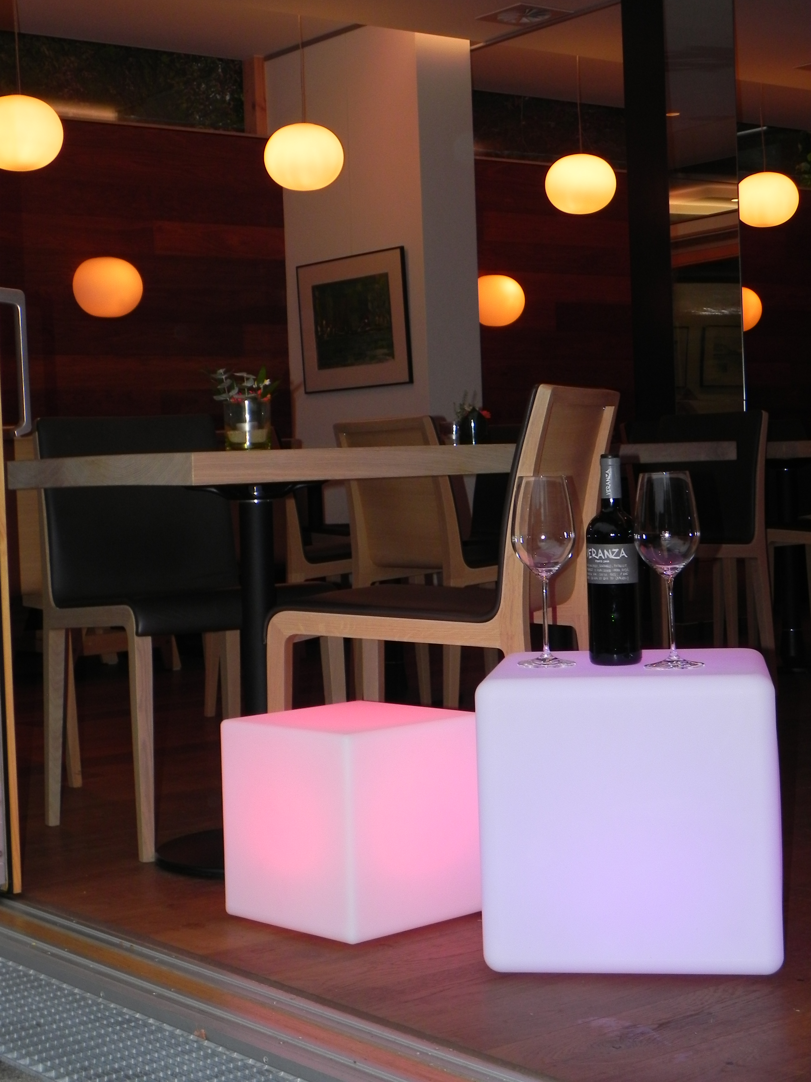 Restaurant-Interieur mit rosa und lila beleuchteten Würfeln, Weingläsern und Hängelampen.