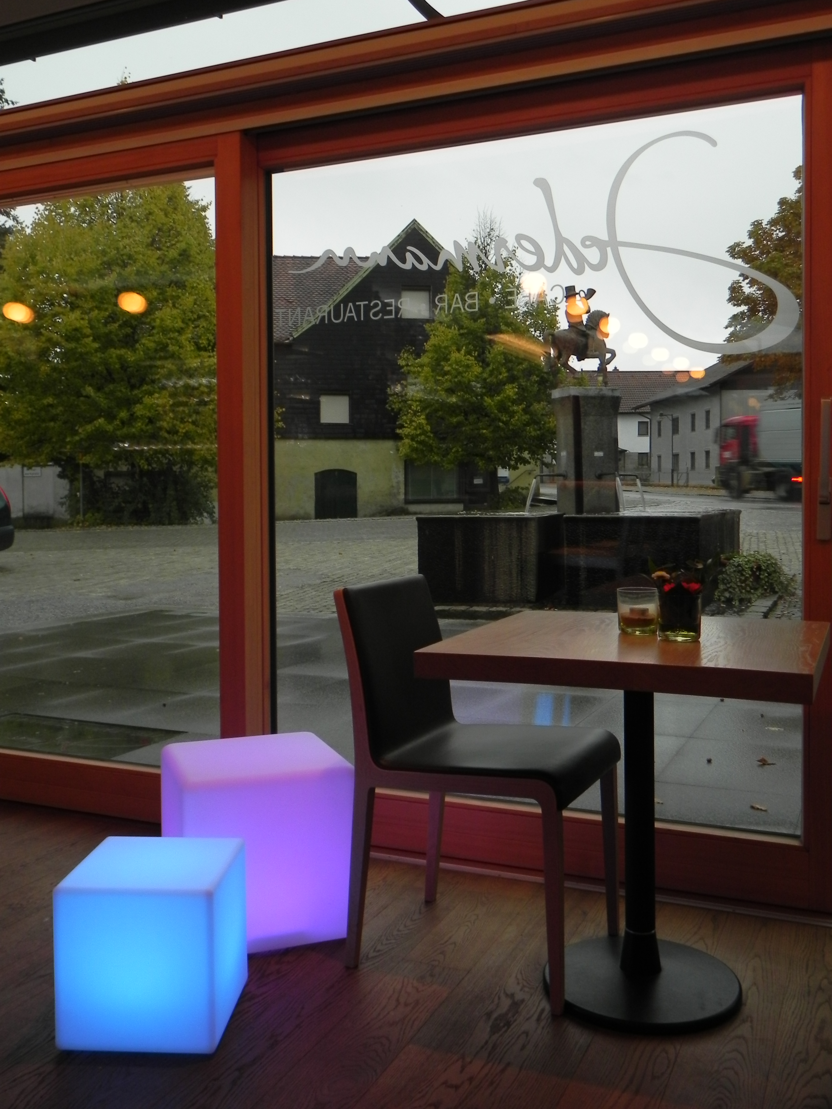 Restaurantinnenraum mit Blick nach draußen. Tische, Stühle und leuchtende Würfel im Vordergrund.
