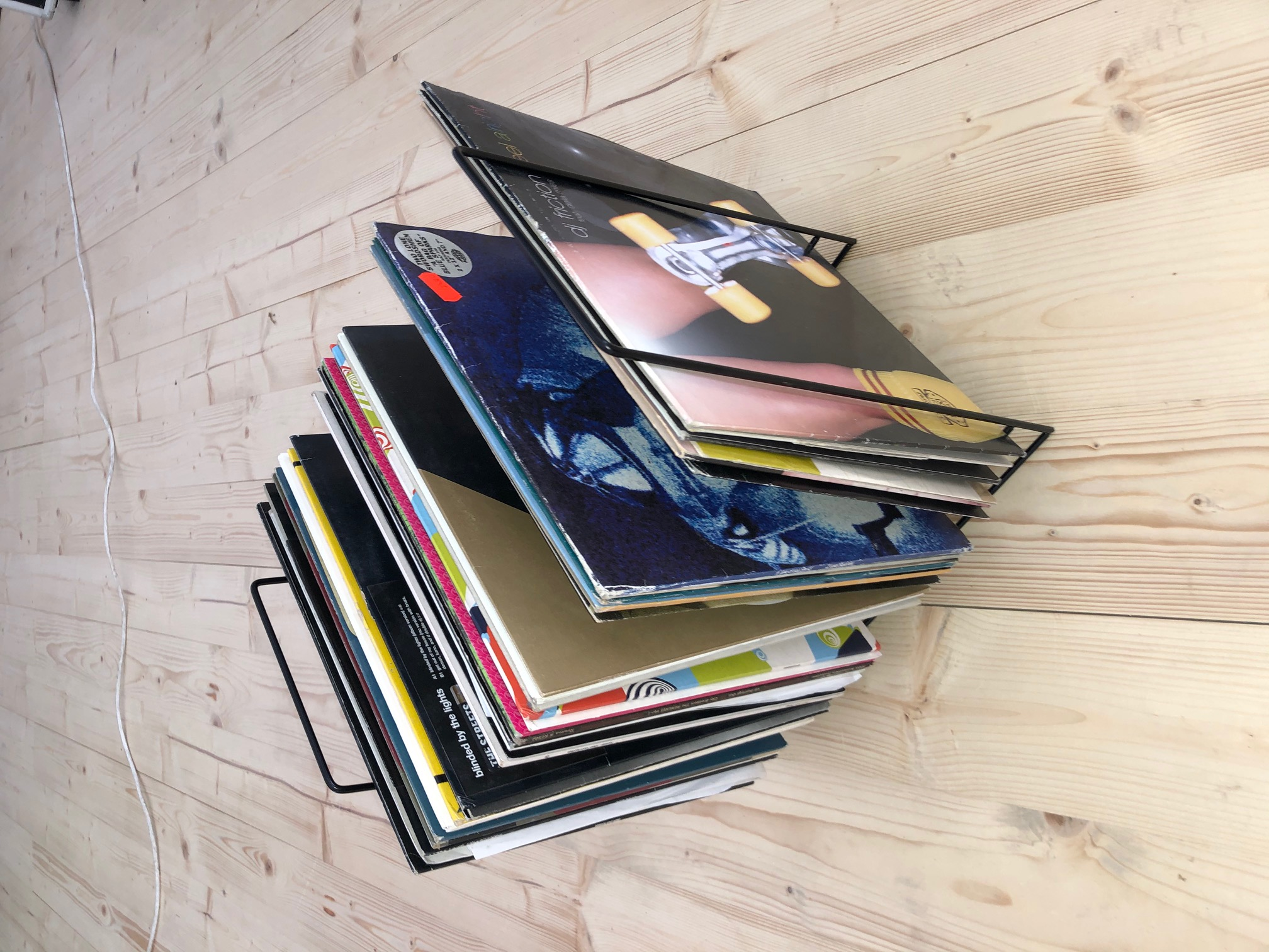 Stapel von Schallplatten in einem schwarzen Gestell auf hellem Holzfußboden. Alben sind sichtbar.