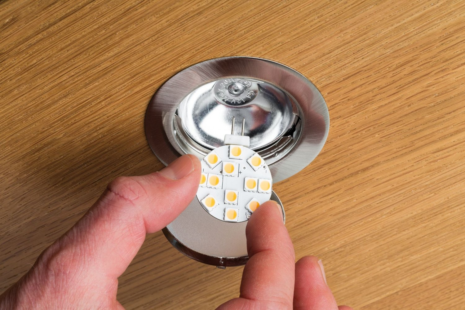 Ręka instalująca małą lampę LED w wpuszczanym oświetleniu sufitowym.