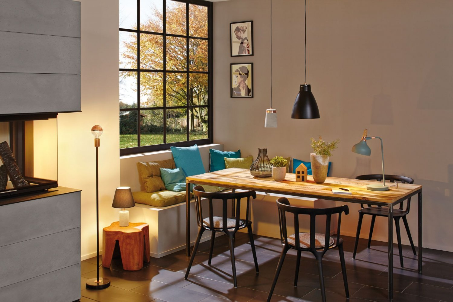 Jadalnia ze stołem z drewna, krzesłami i oknem, przez które widać drzewo z jesiennymi liśćmi.